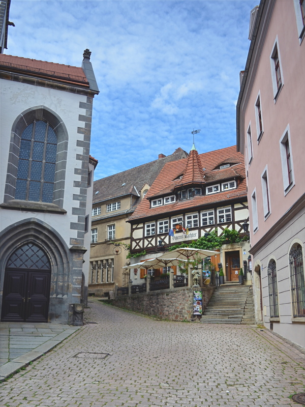 2 - A cobblestone lane in the historic old town of Meißen, Germany, featuring the Frauenkirche (Church of Our Lady) on the left and the half-timbered Restaurant Vincenz Richter building
